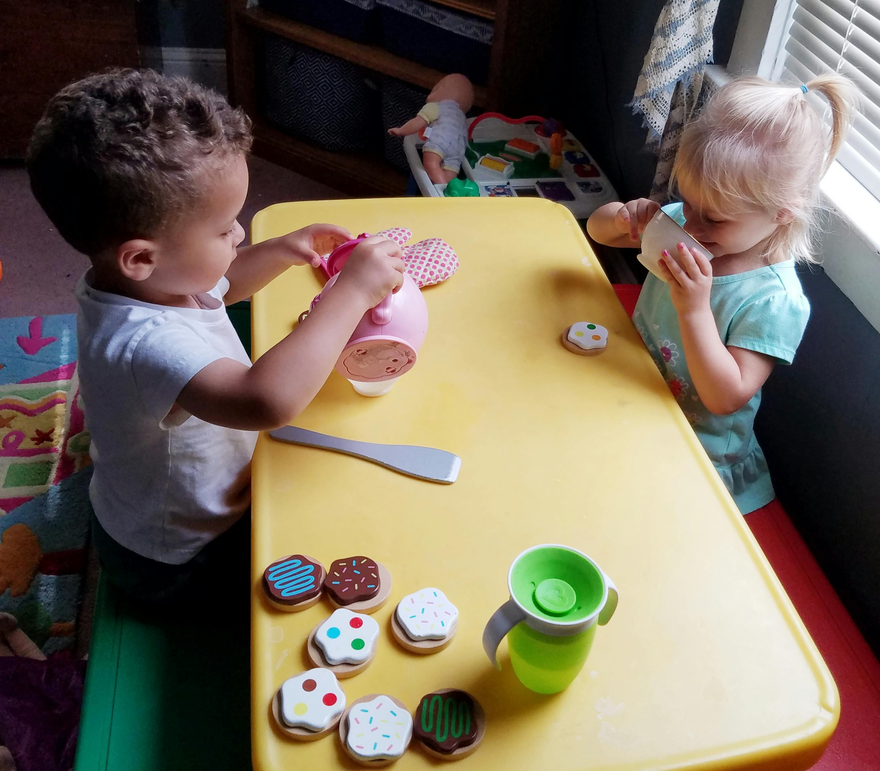 Two children playing with toy food at a yellow table