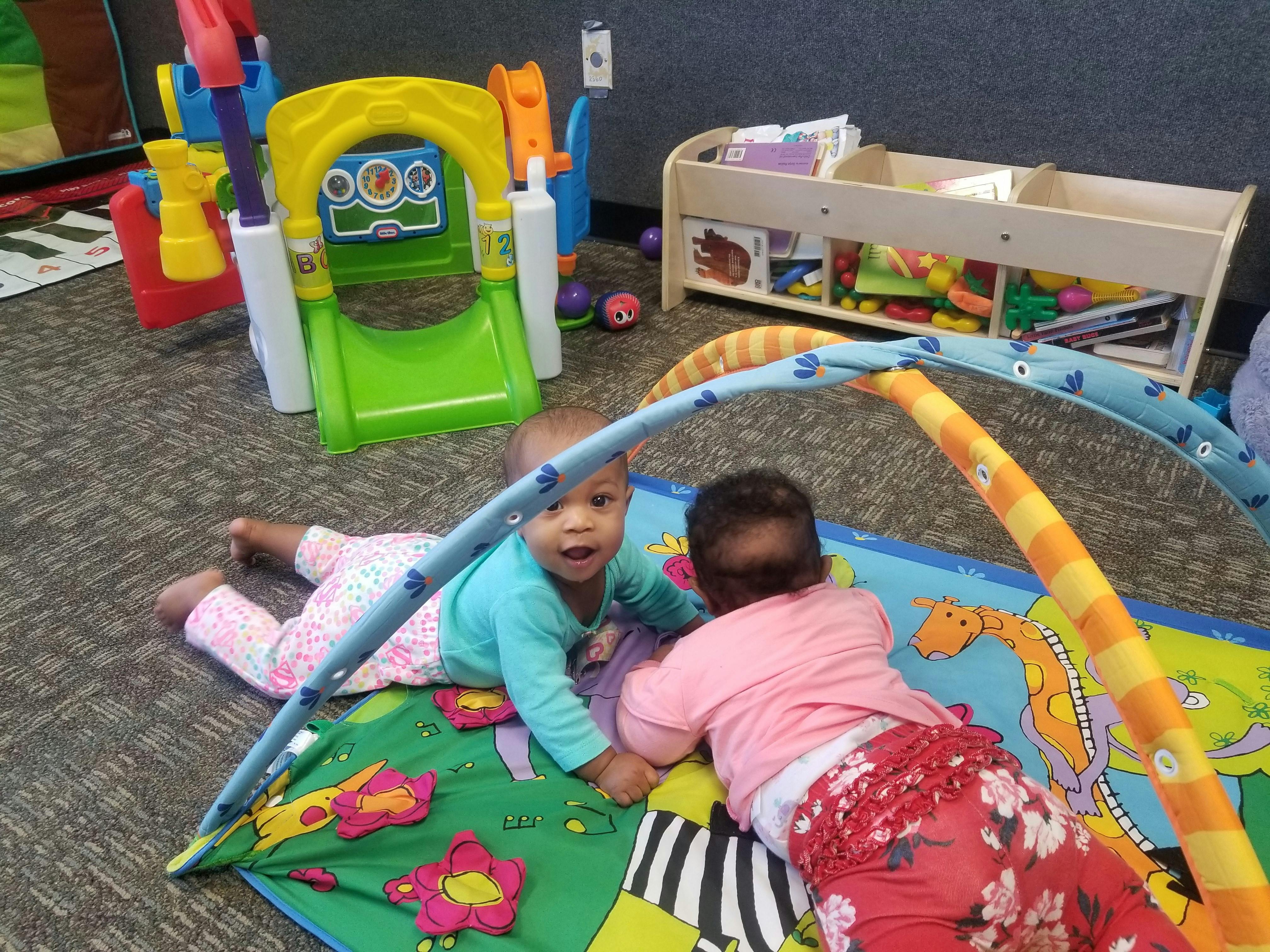 Two children playing on a colorful mat with an activity arch