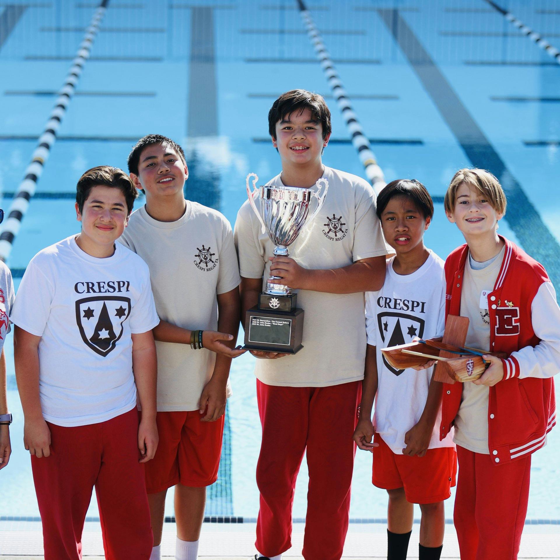 Five teens holding a trophy and wooden boats by a swimming pool