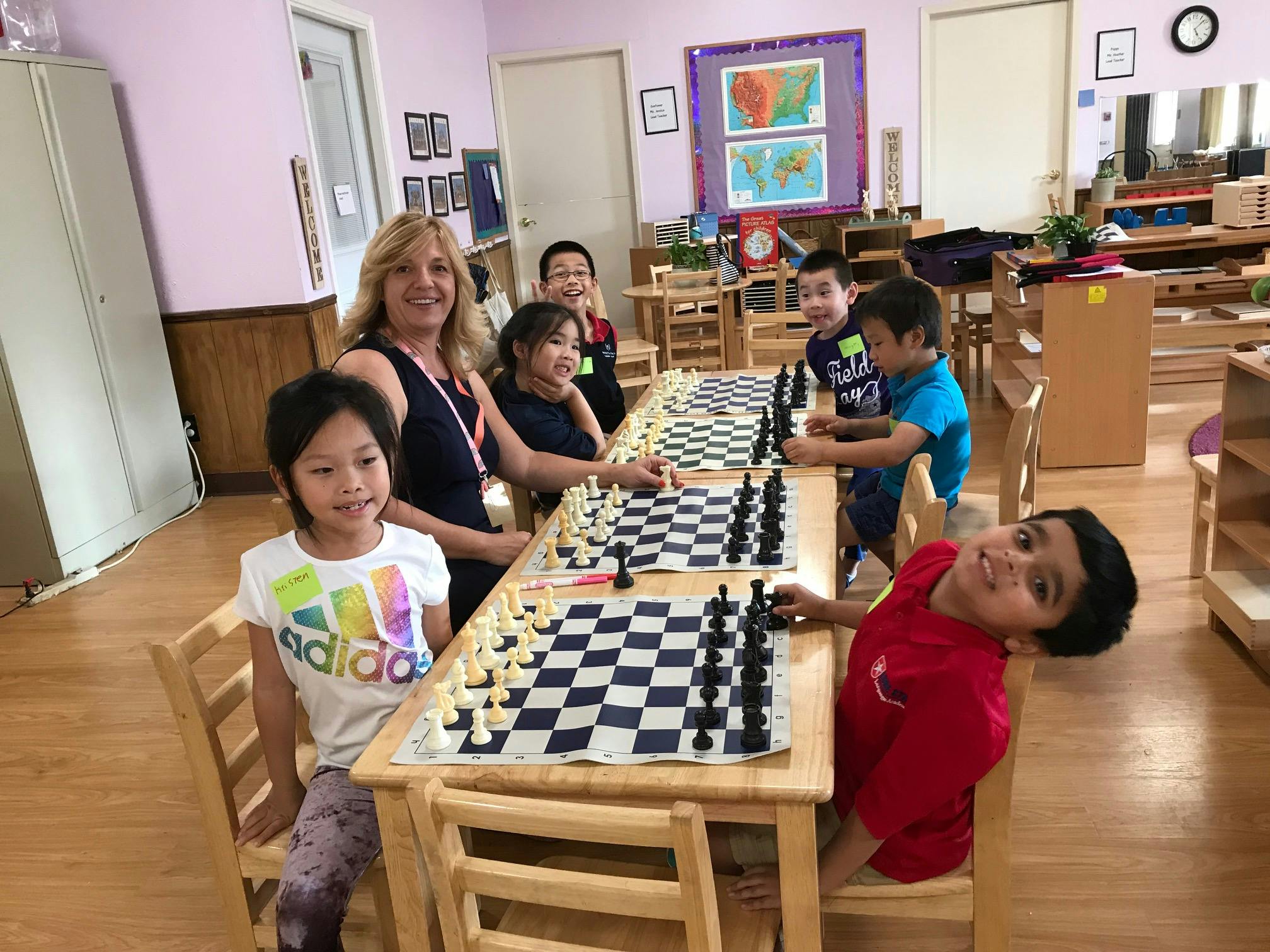 Adult and children playing chess at tables in a classroom