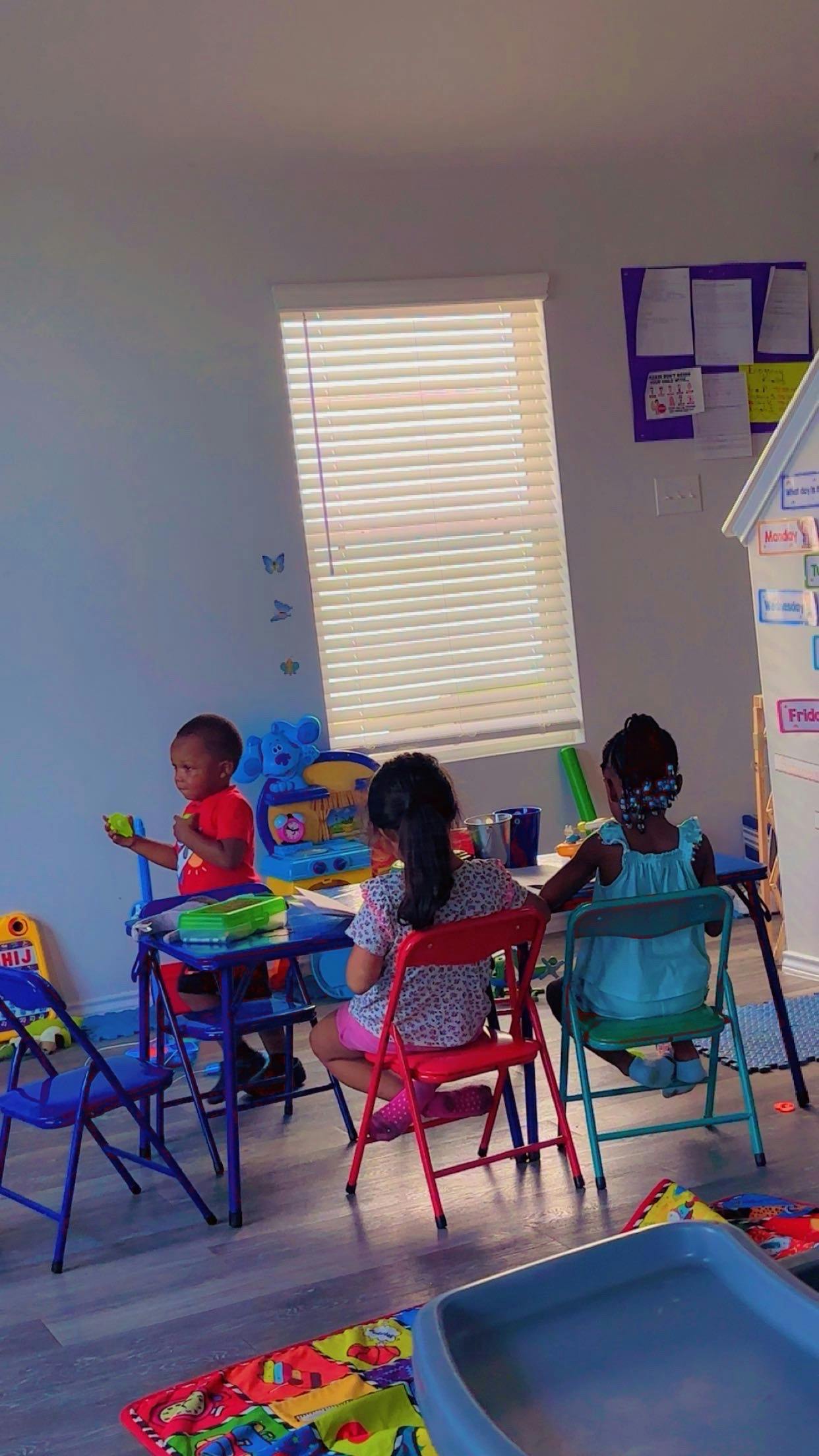 Three children sitting at desks in a playroom