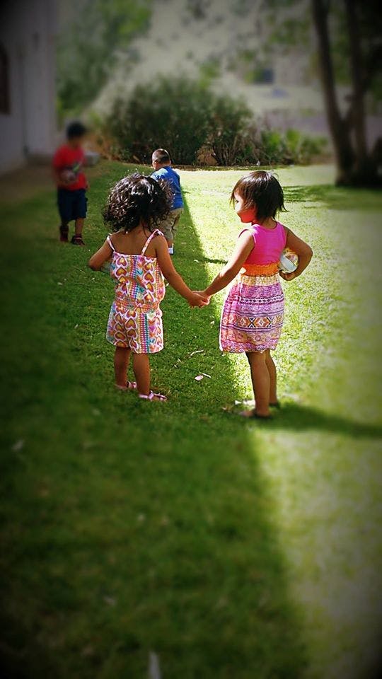 Two children holding hands on grass, with other children in background