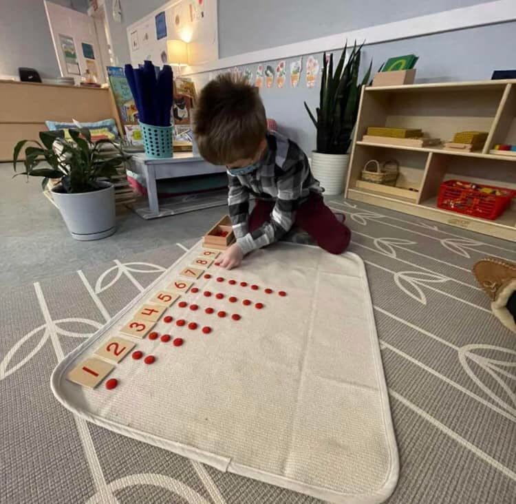 Child kneeling on a rug, arranging red counters next to number tiles