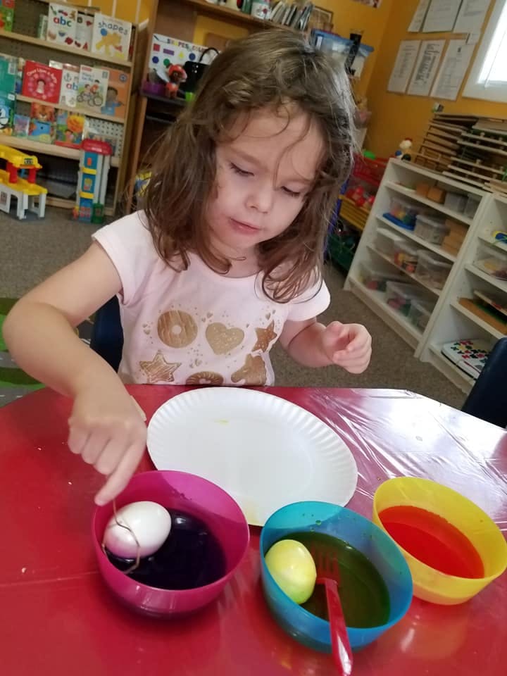 Child dyeing an egg in a bowl of liquid
