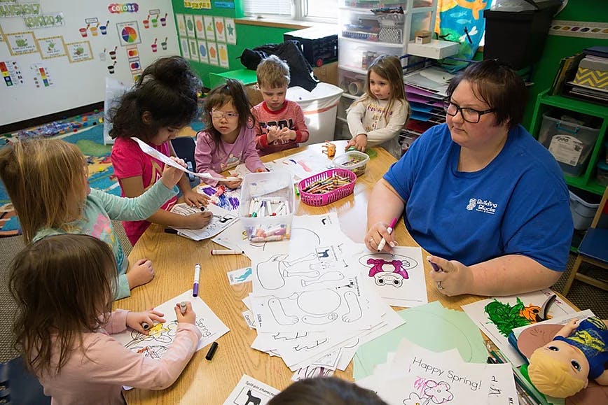 Adult and children coloring at a table in a classroom