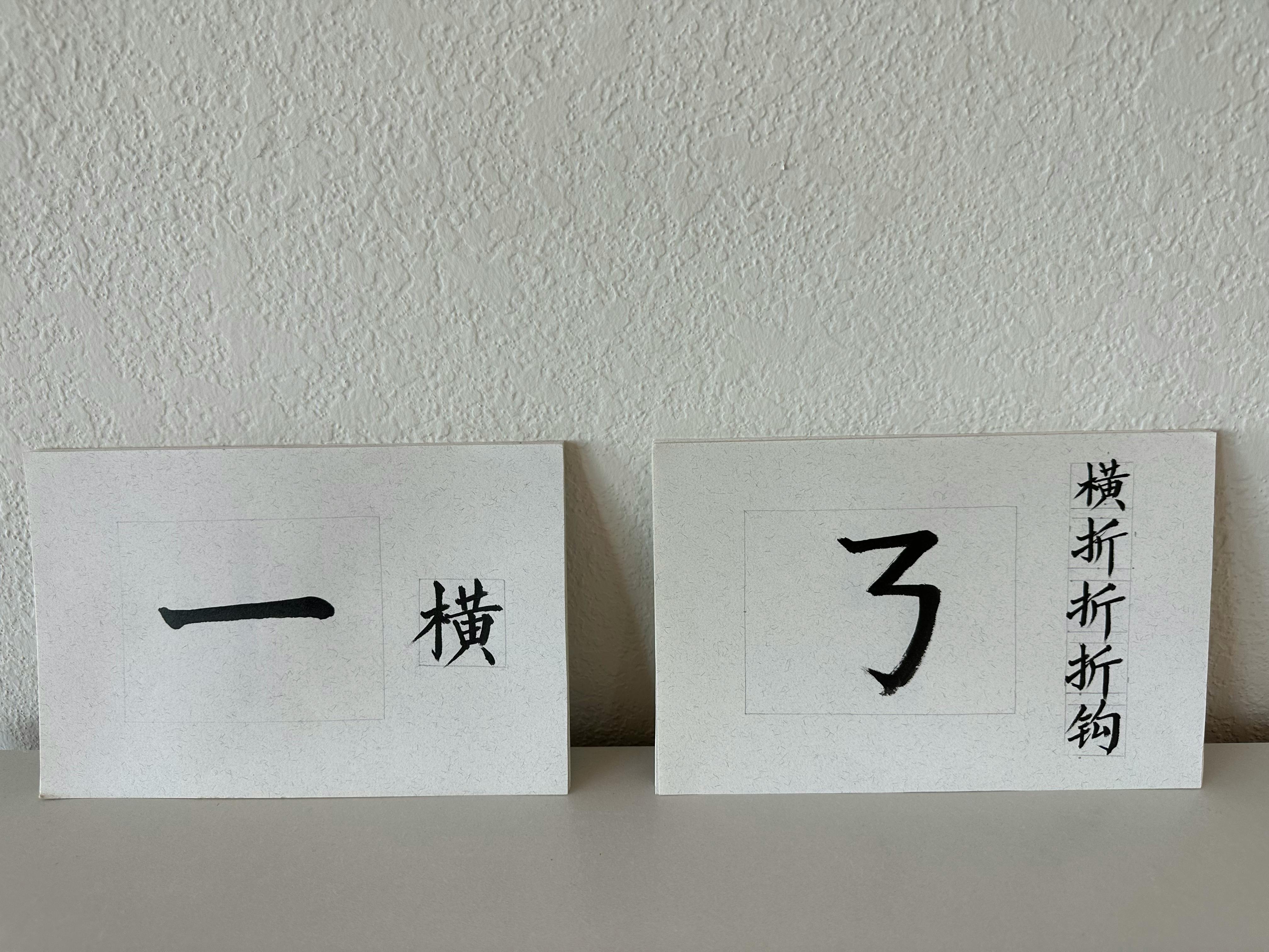 Two white cards with black calligraphy, one with a horizontal stroke and text, the other with a character resembling '3' and vertical text