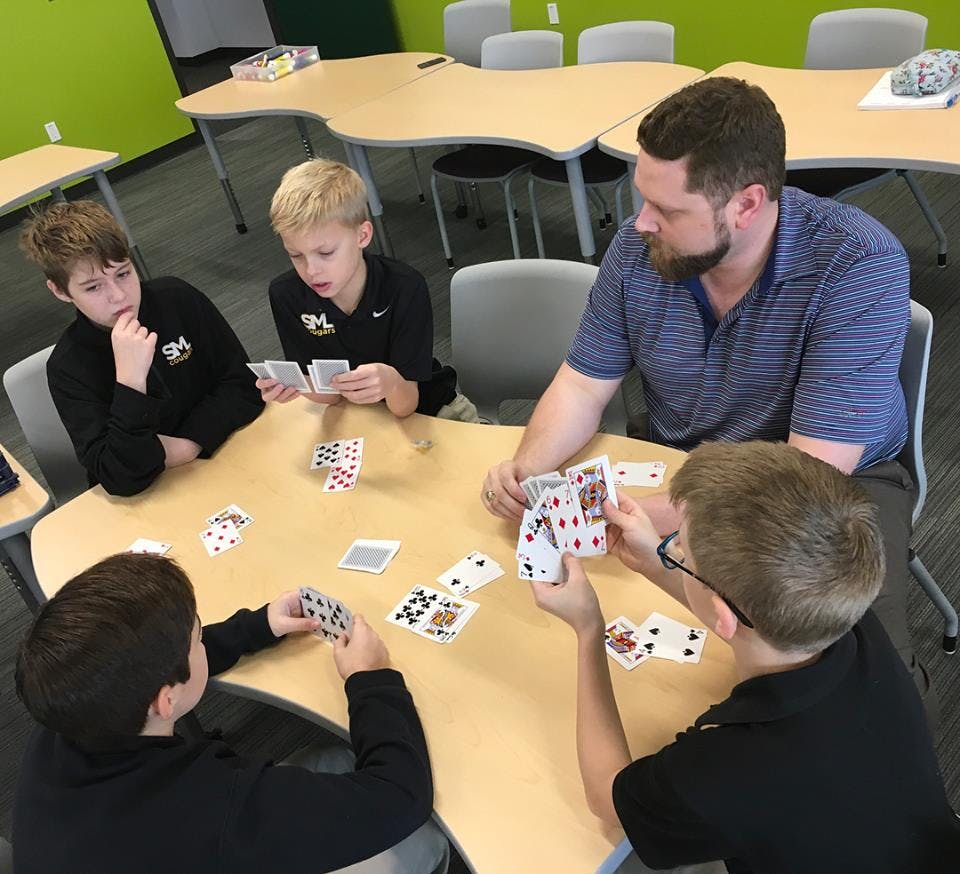 Adult and three children playing cards at a table