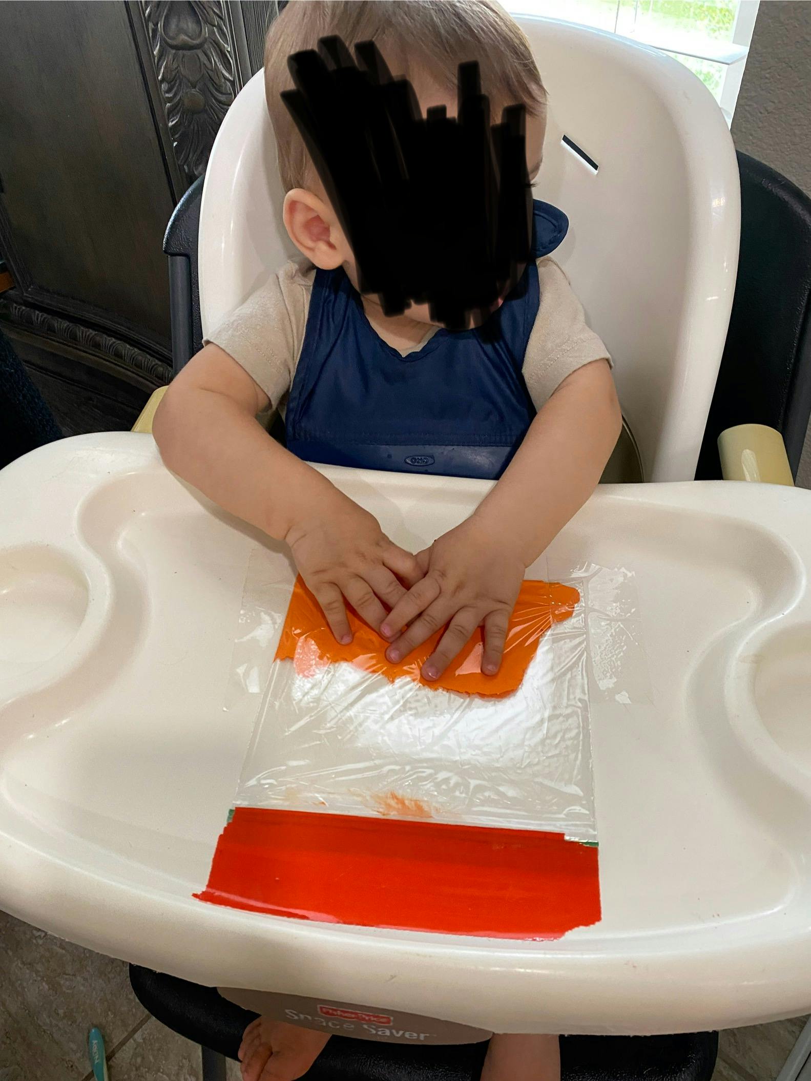 Child in a high chair playing with a plastic bag containing orange paint