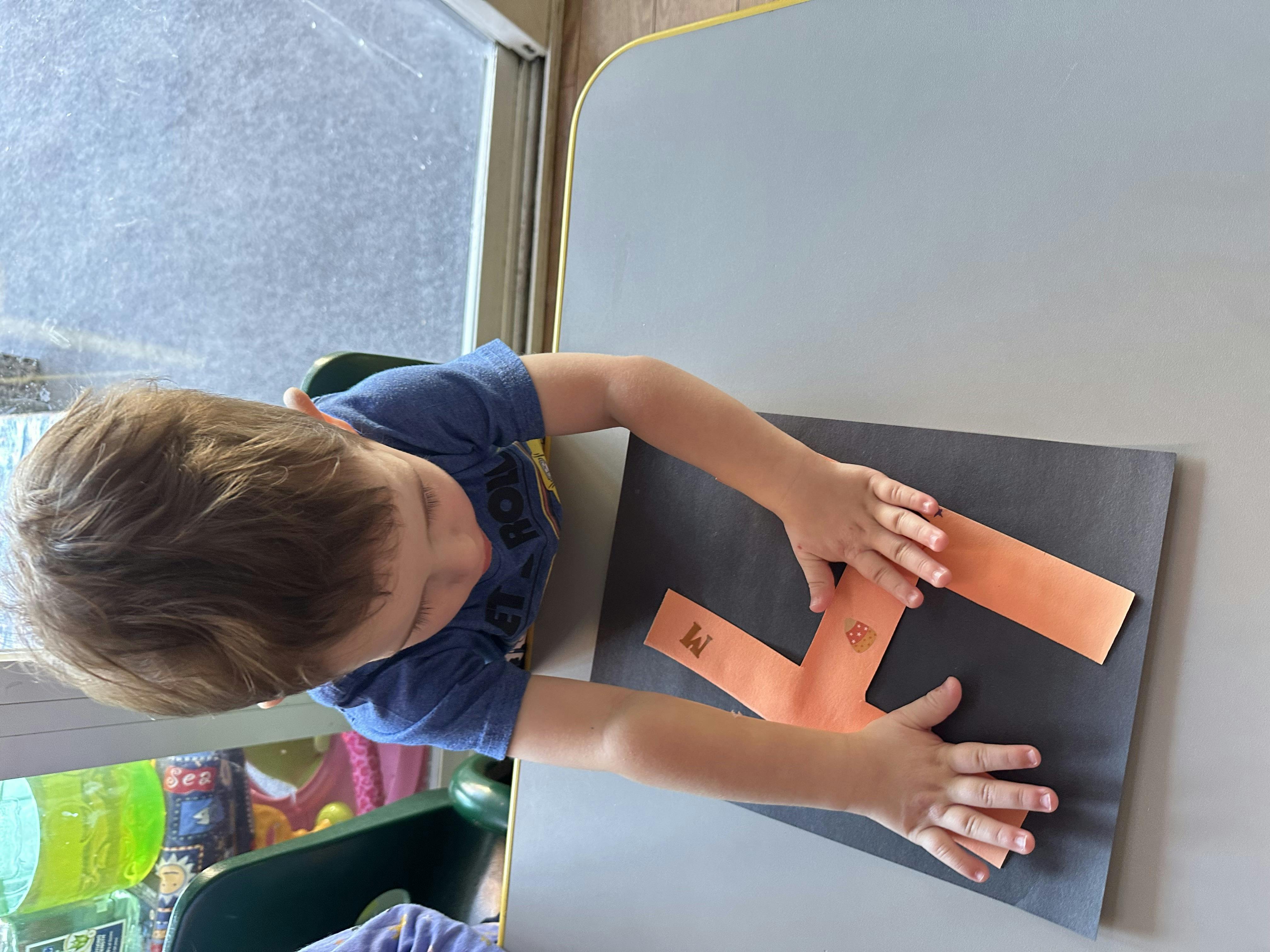 Child at a table with hands on orange paper strips on a dark mat