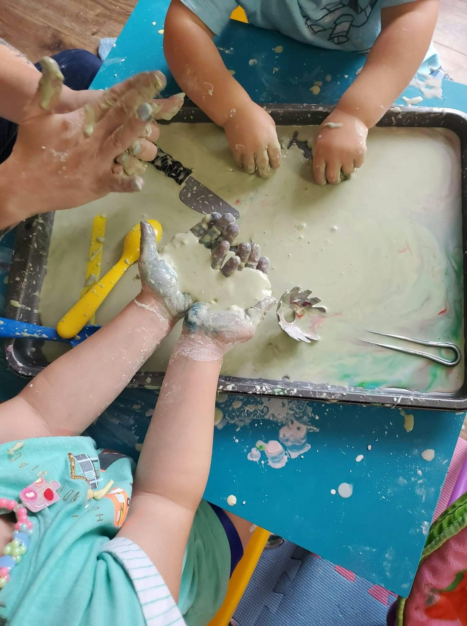 Multiple people's hands playing with a messy substance in a tray