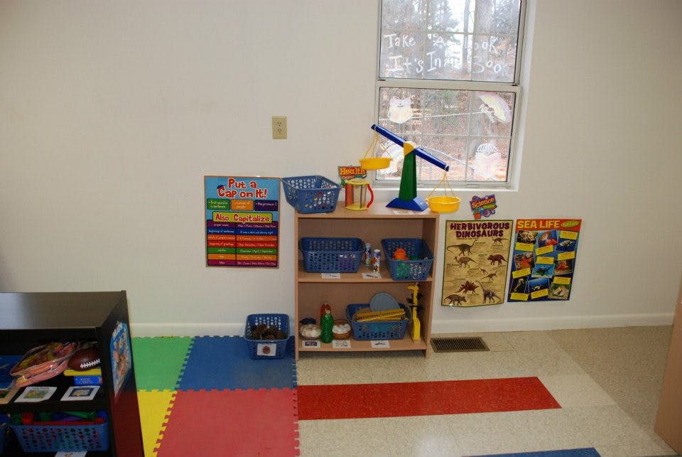 Classroom with colorful floor mats, shelves with toys, and posters on the wall