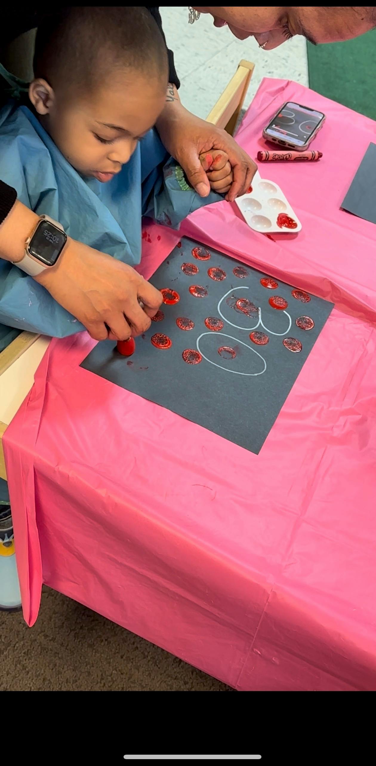 Person and child painting on paper with red paint on a dark paper