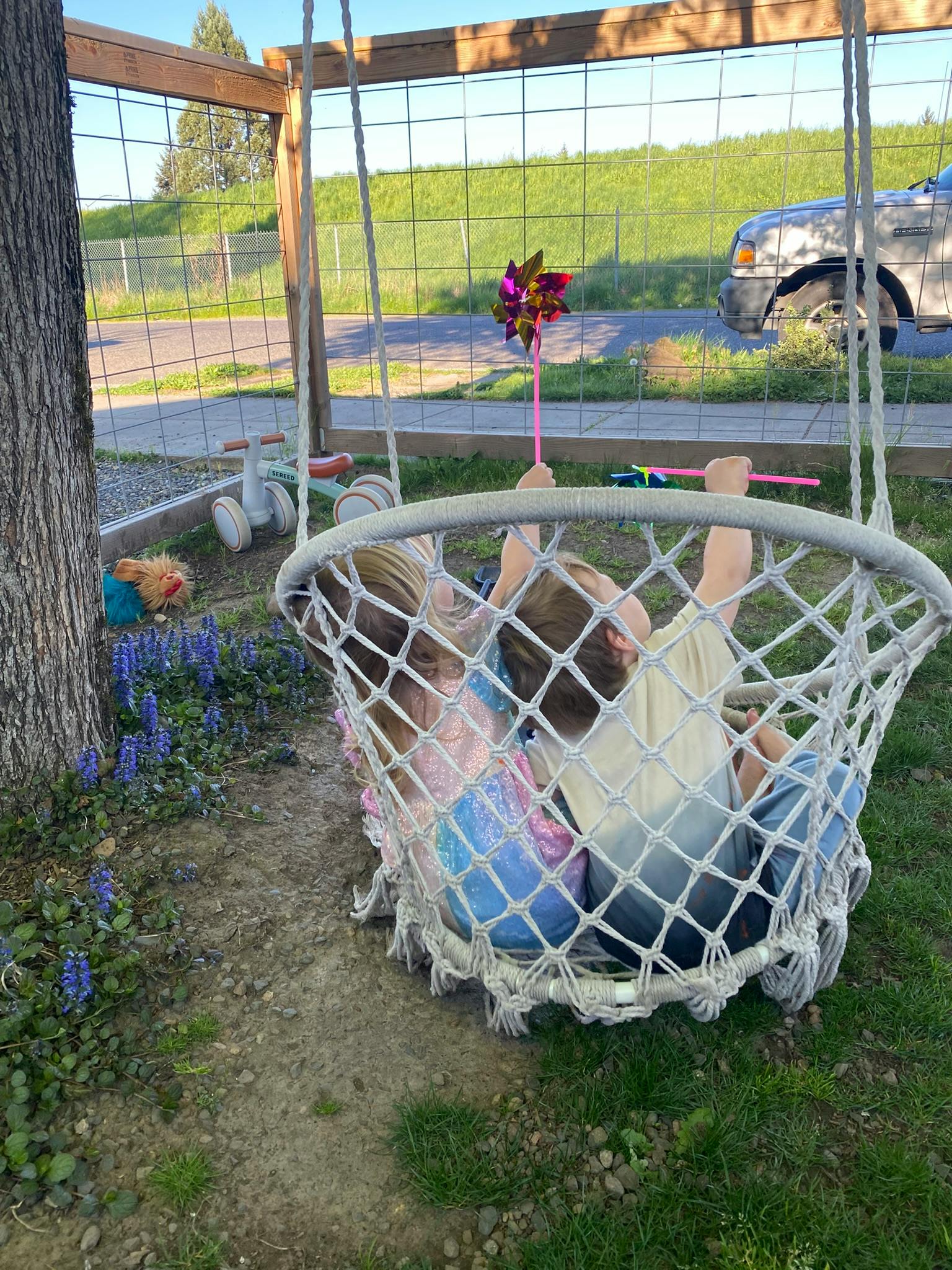 Two children sitting in a net swing, one holding a pinwheel