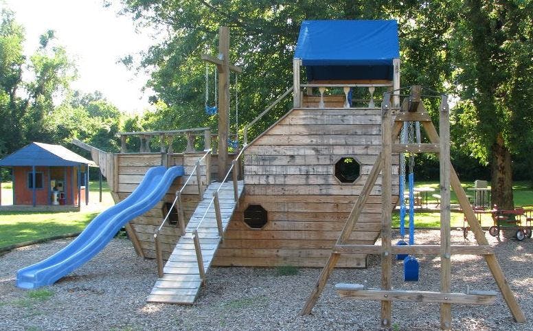 Wooden playground structure shaped like a ship with a blue slide