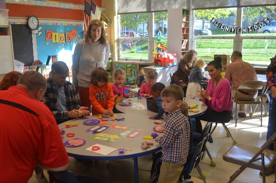 Adults and children gathered around tables in a classroom