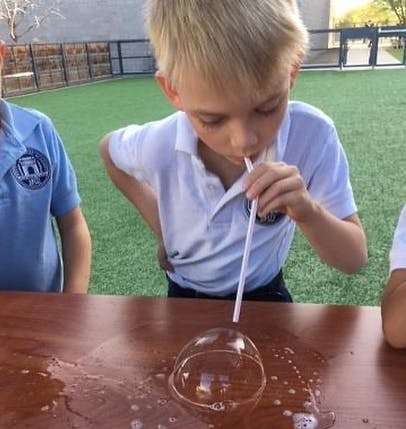 Child blowing a bubble with a straw on a wooden table