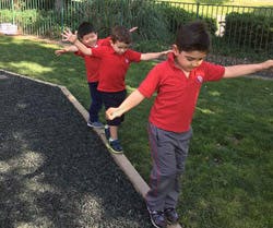 Three children balancing on a low beam outdoors