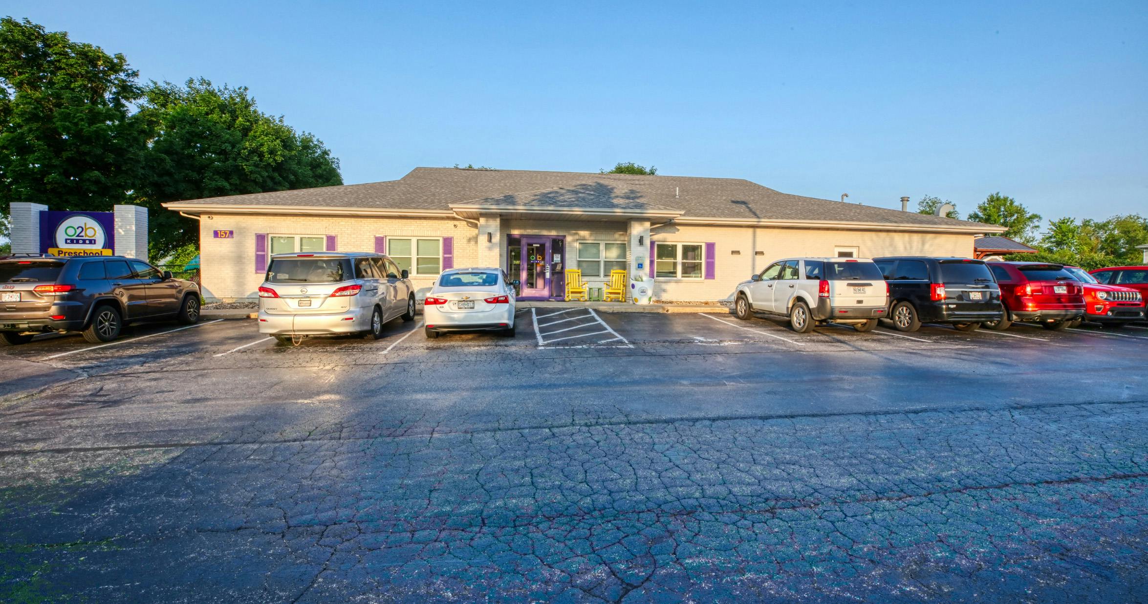 Building with "O2B Kids Preschool" sign and a parking lot with cars