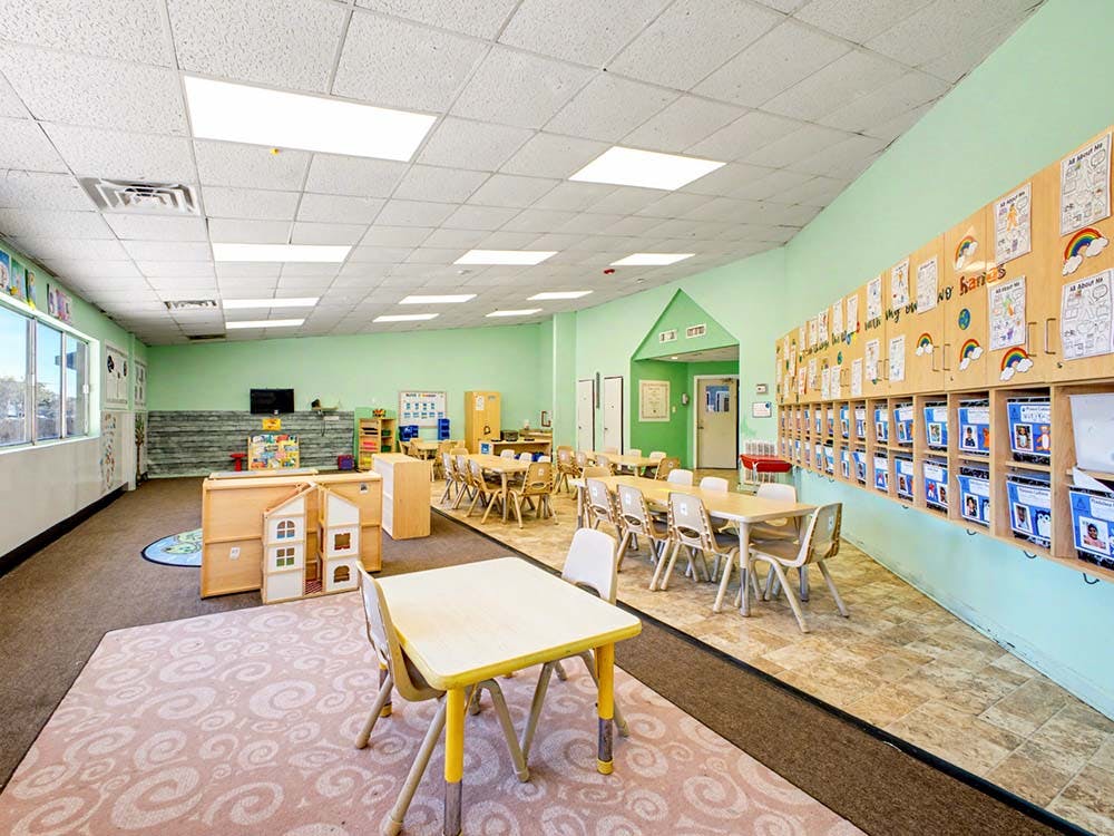 Classroom with child-sized tables and chairs, play furniture, and cubbies with artwork