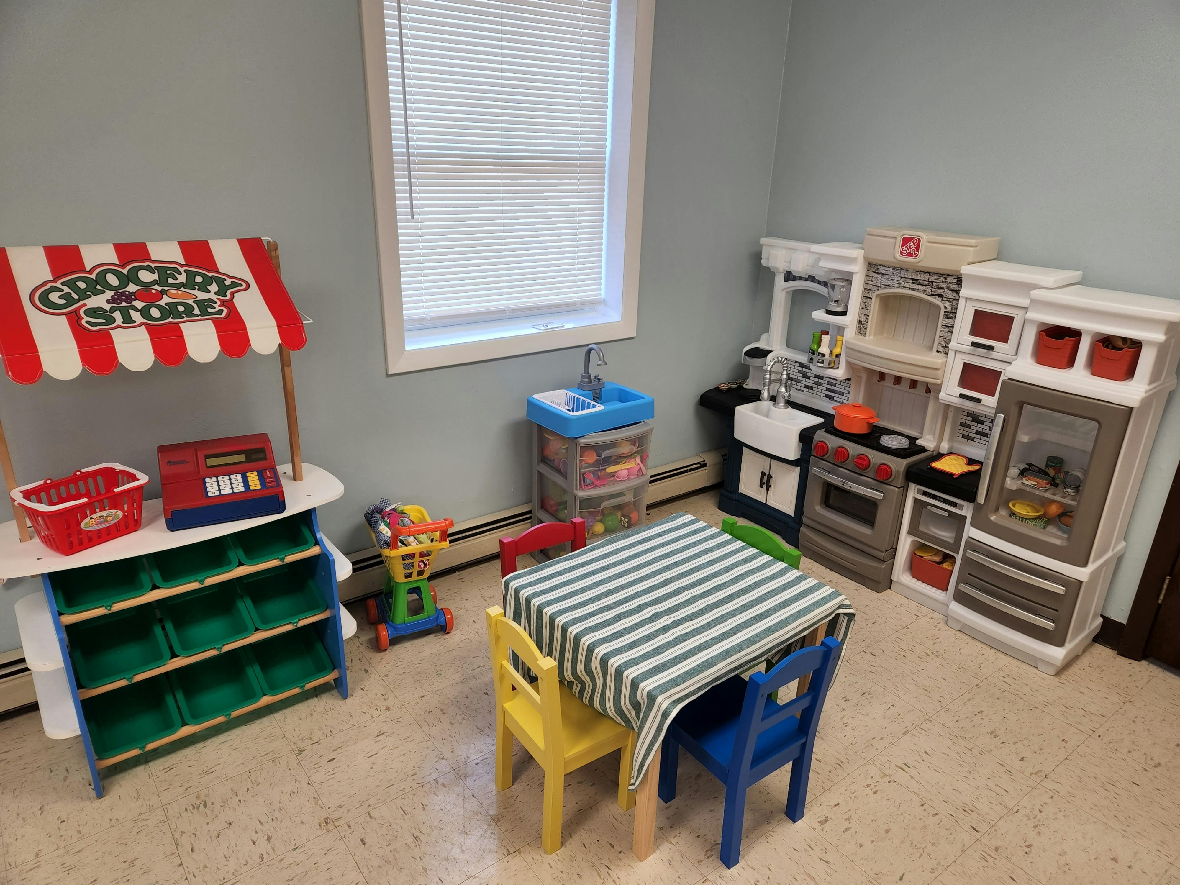 Playroom with toy grocery store, kitchen set, and small table with chairs