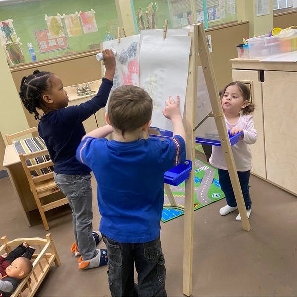 Three children drawing on an easel in a classroom