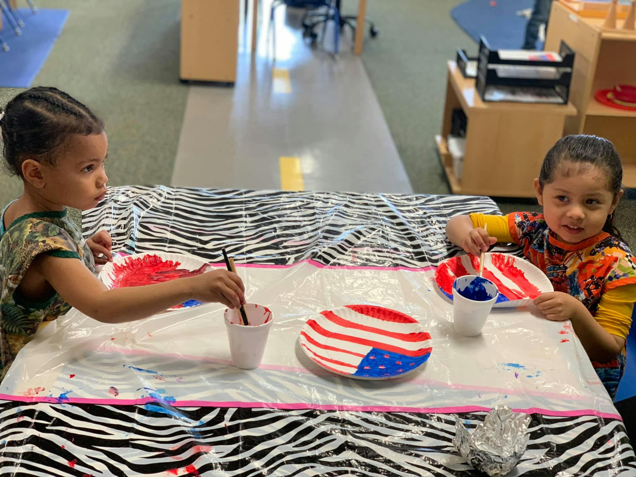 Two children painting paper plates with red, white, and blue colors