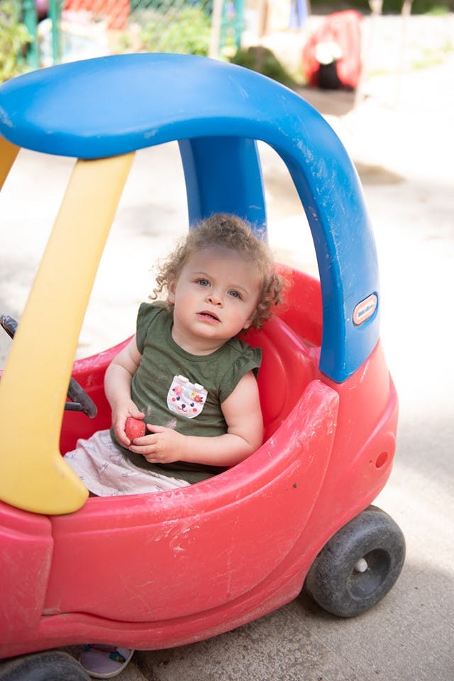 Child in a toy car holding a small red object