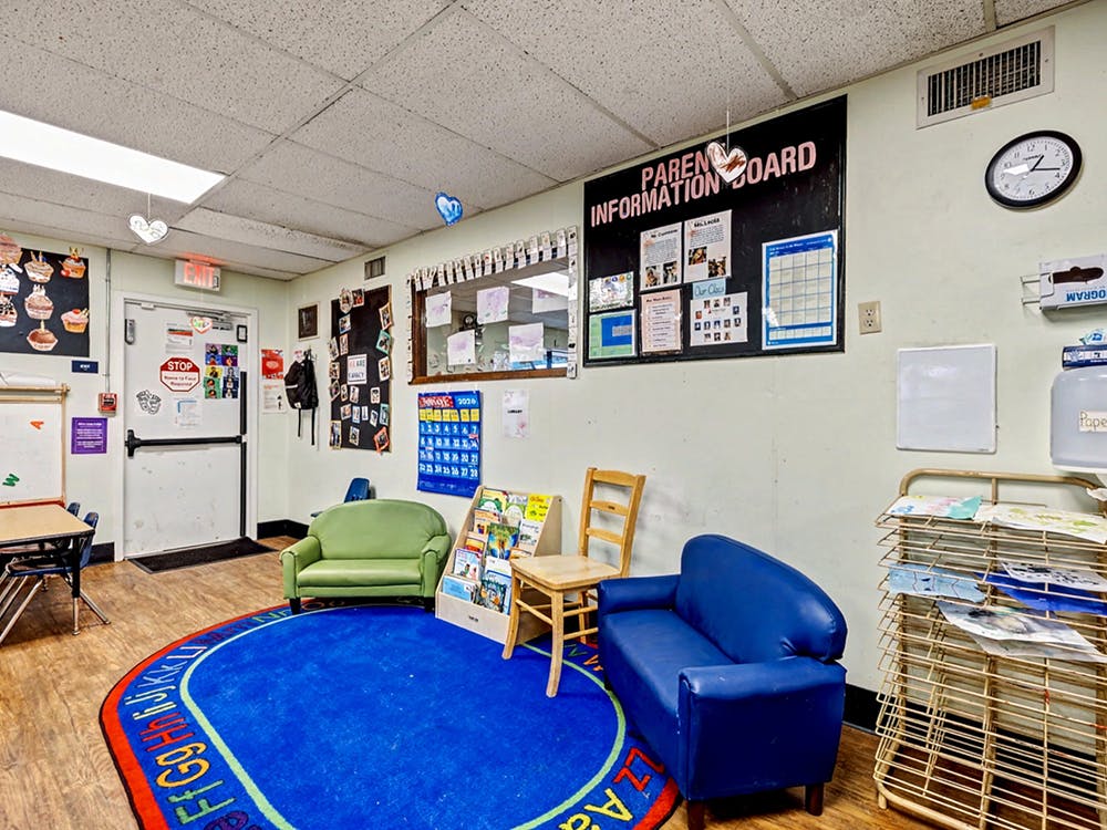 Classroom with a blue rug, small sofas, and a parent information board