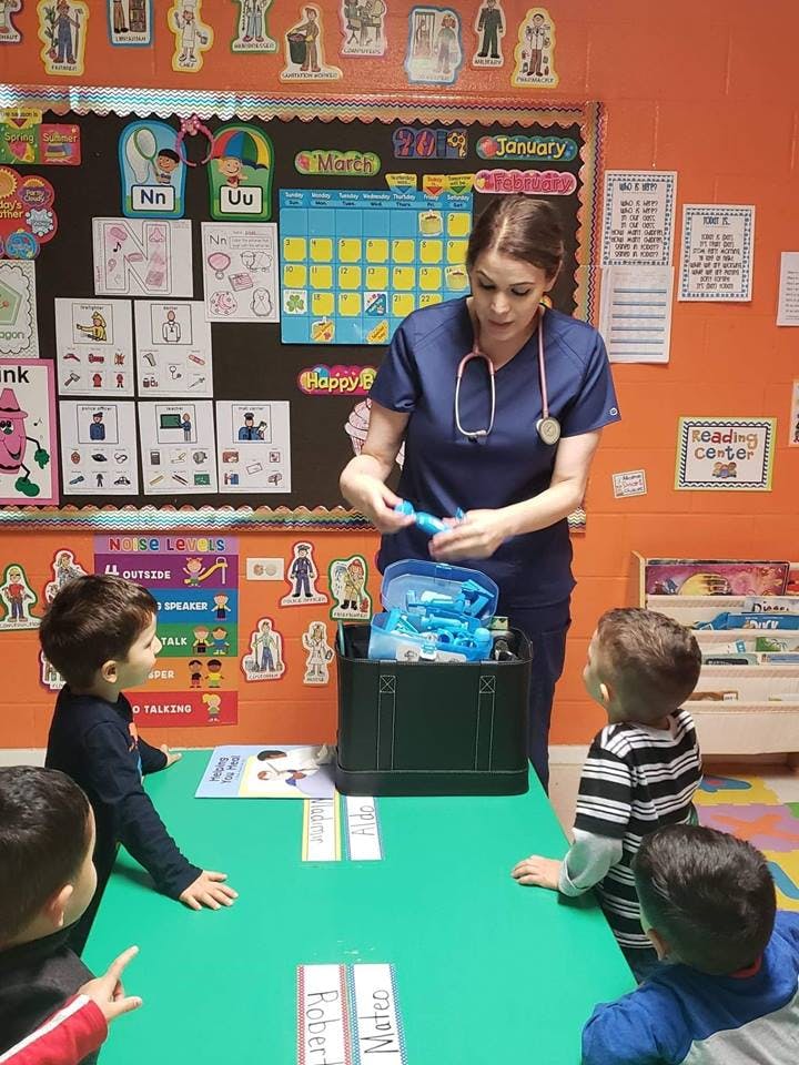 Person in scrubs with stethoscope showing items to children in a classroom