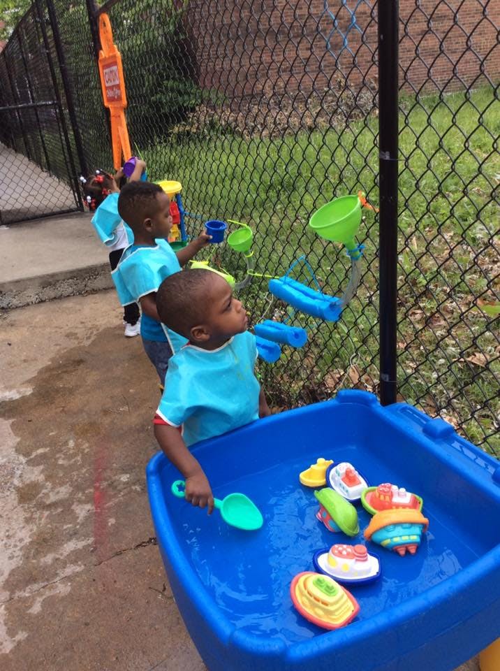 Children playing with water toys at a fence-mounted activity station