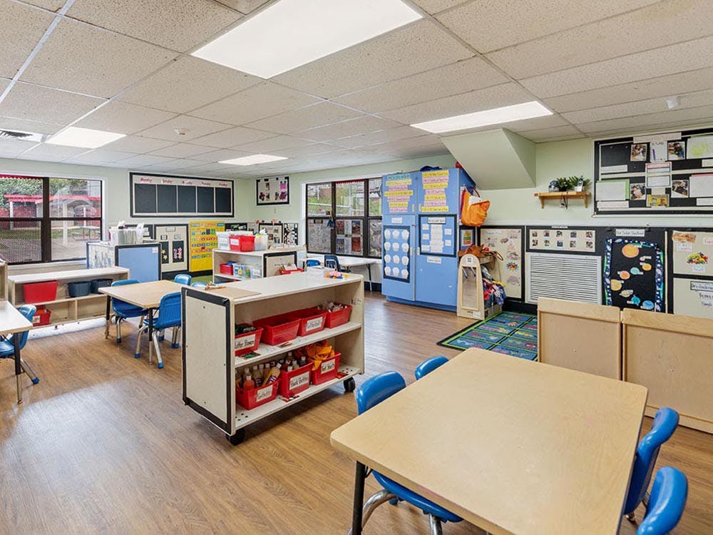 Empty classroom with small tables and chairs, shelves with red bins