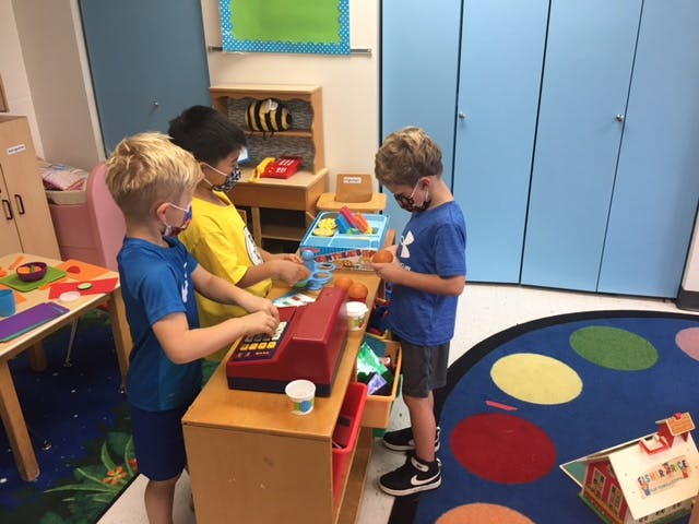 Three children playing with a toy cash register and other toys in a classroom