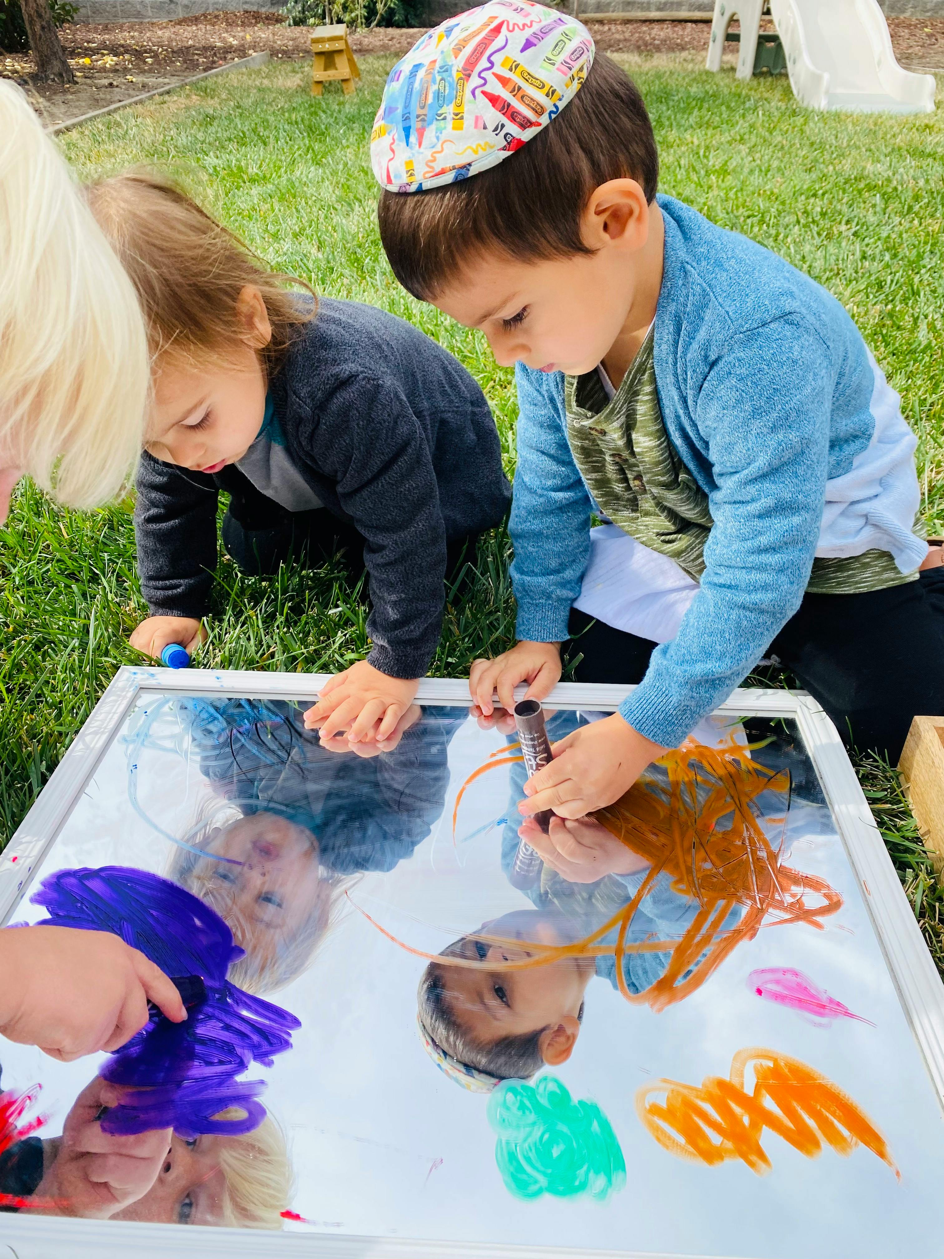 Two children drawing on a mirror with paint
