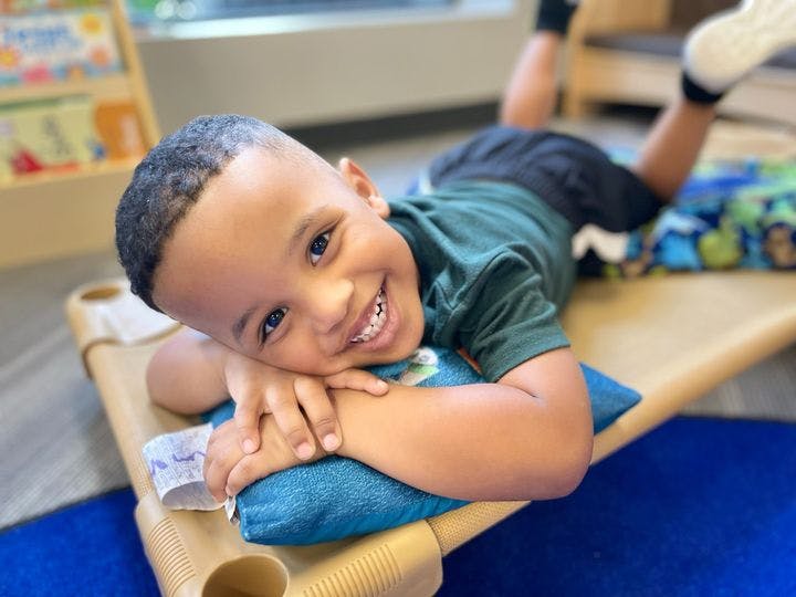 Child lying on a cot with head on a pillow, smiling