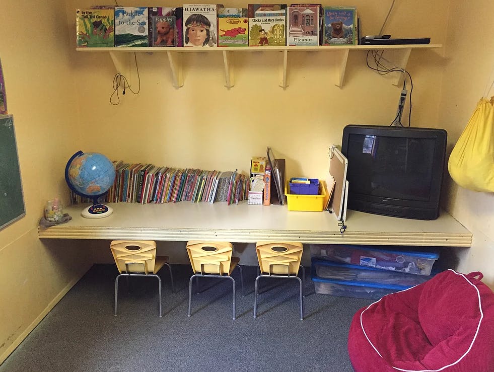 Classroom with a desk, three chairs, books, a globe, and a television