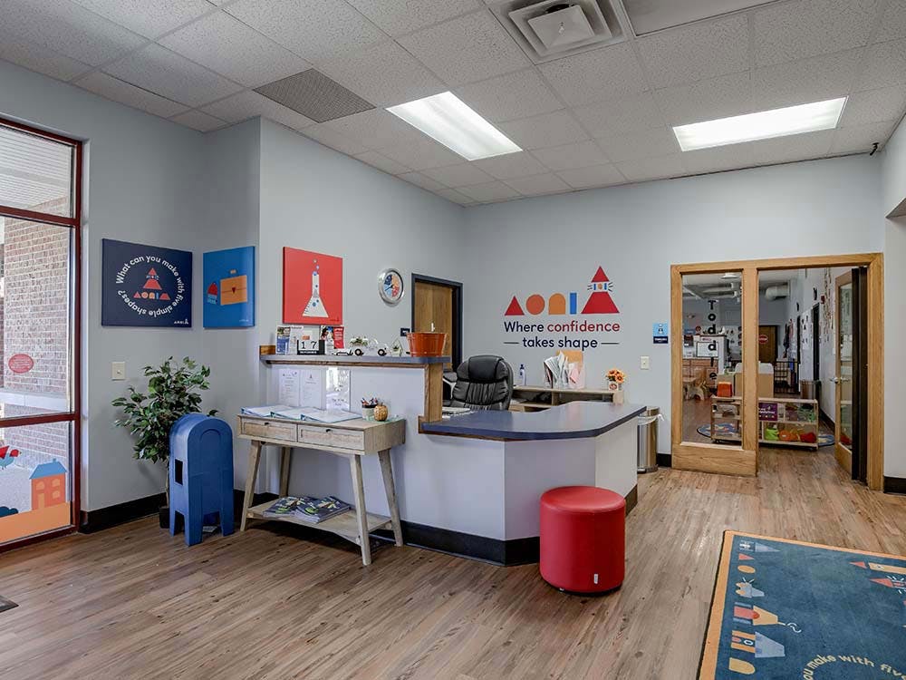 Reception area with a desk, red stool, and a door leading to a classroom