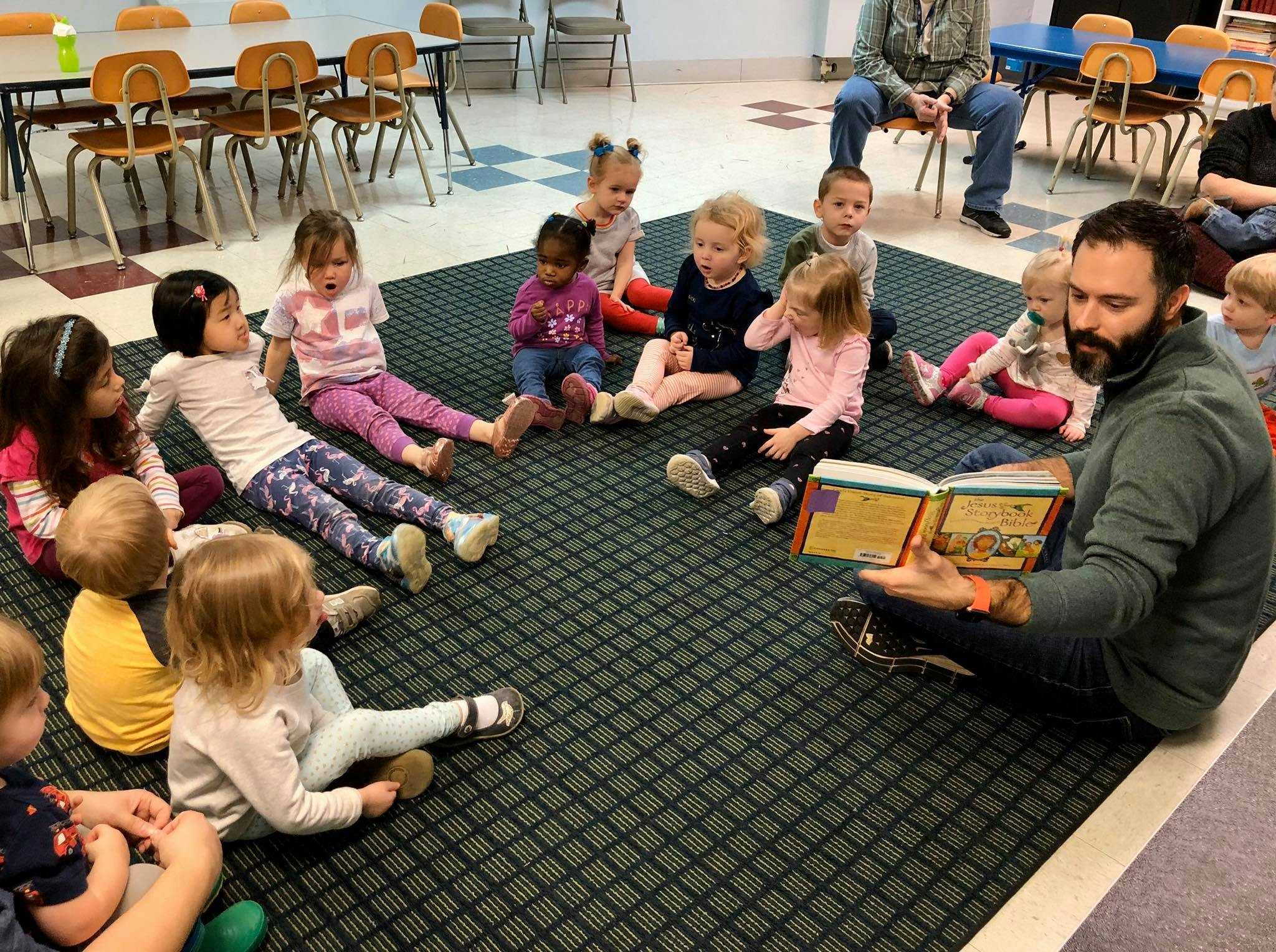 Adult reading a book to a group of children sitting on a rug