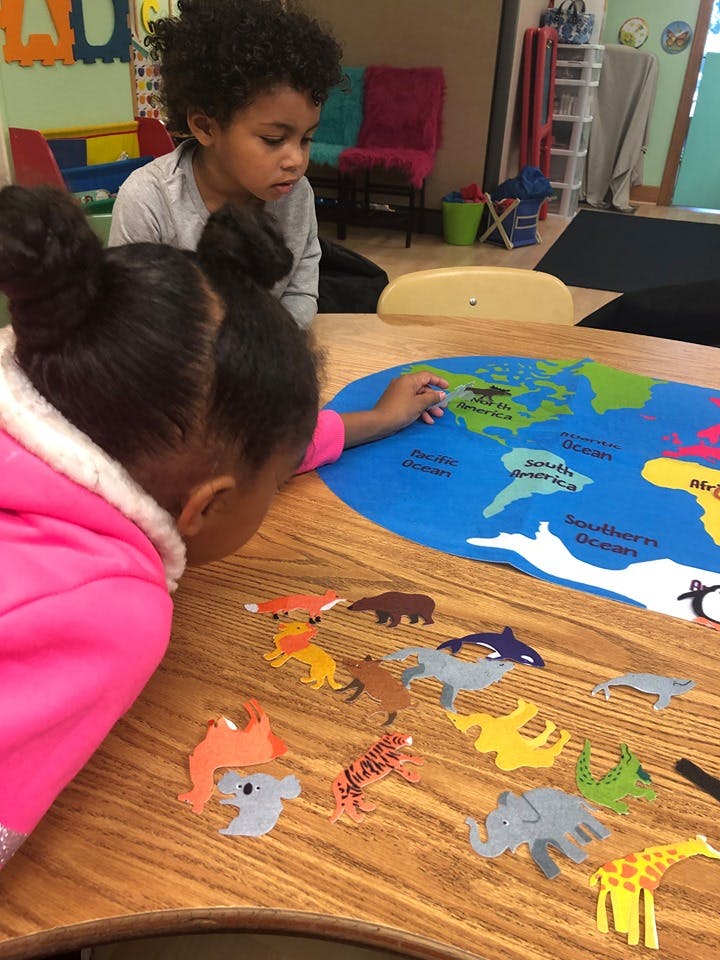 Two children playing with animal cutouts on a world map