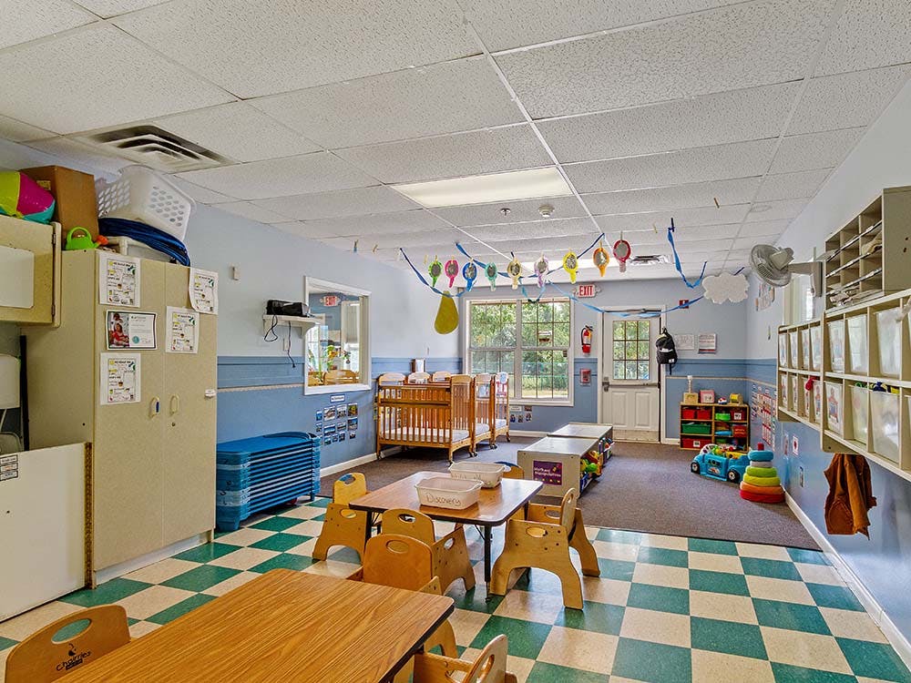 Empty children's classroom with small tables and chairs, cribs, and toys