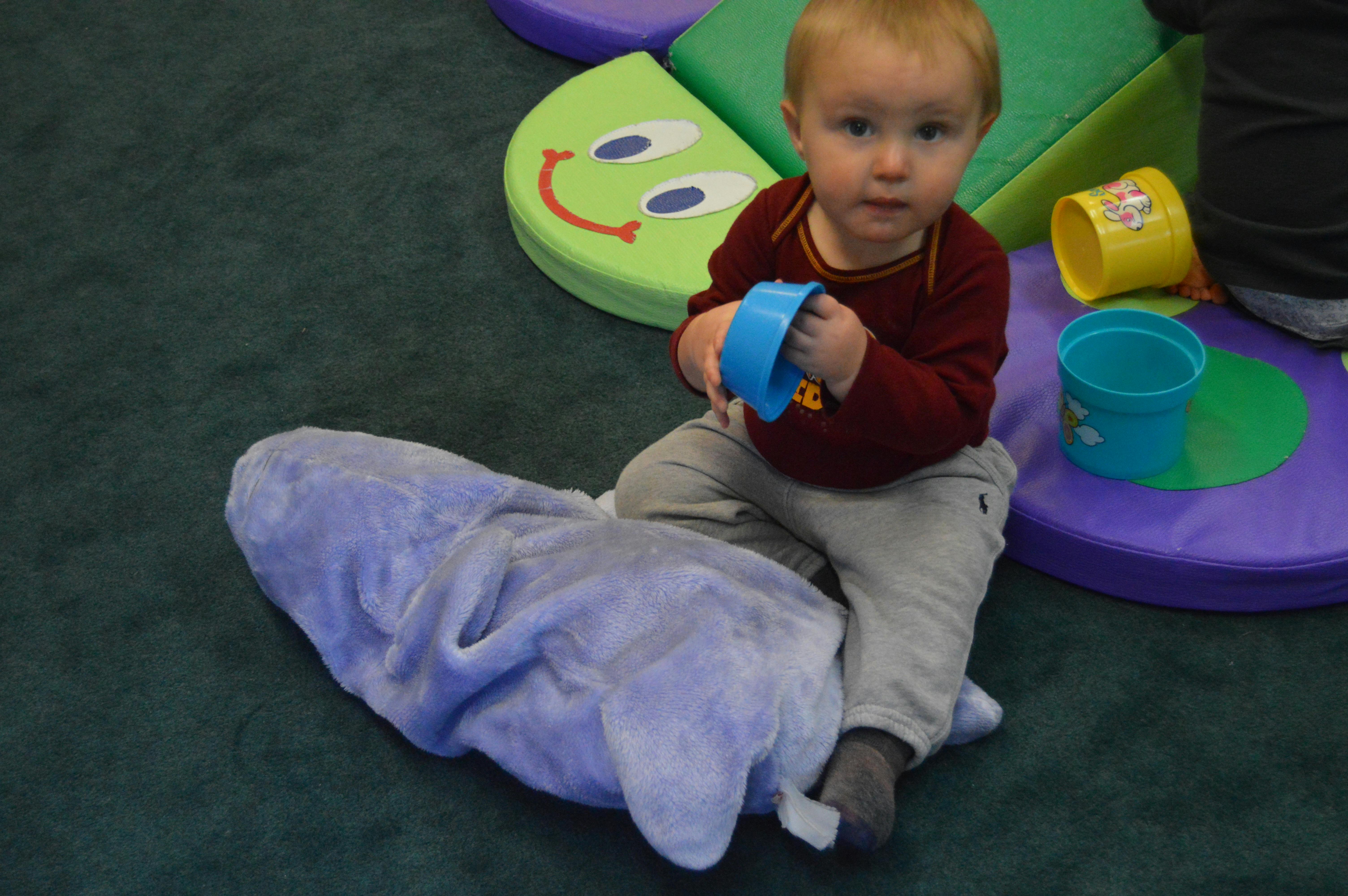 Child sitting on a purple stuffed animal holding a blue toy