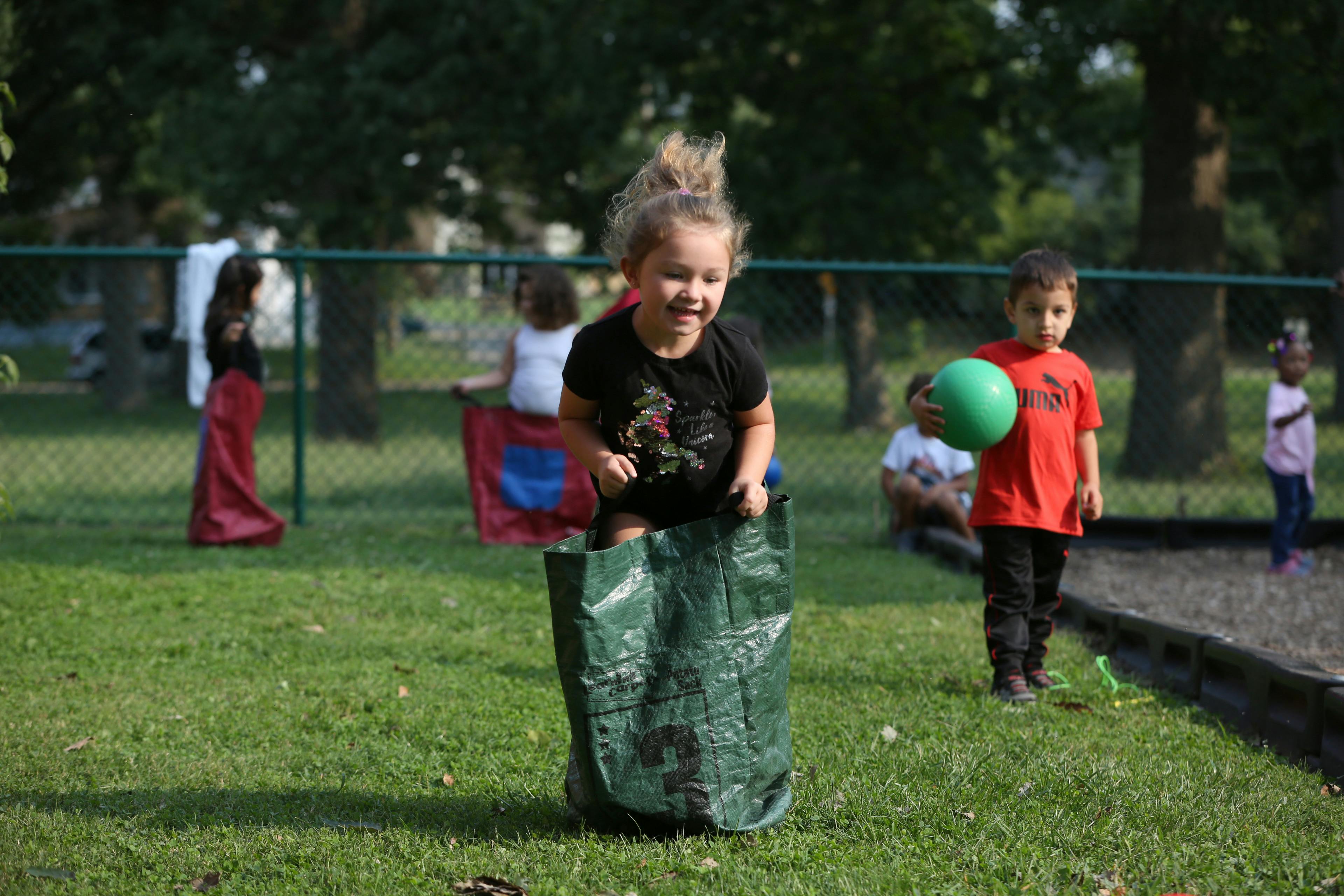 Child in a sack race on grass with other children nearby