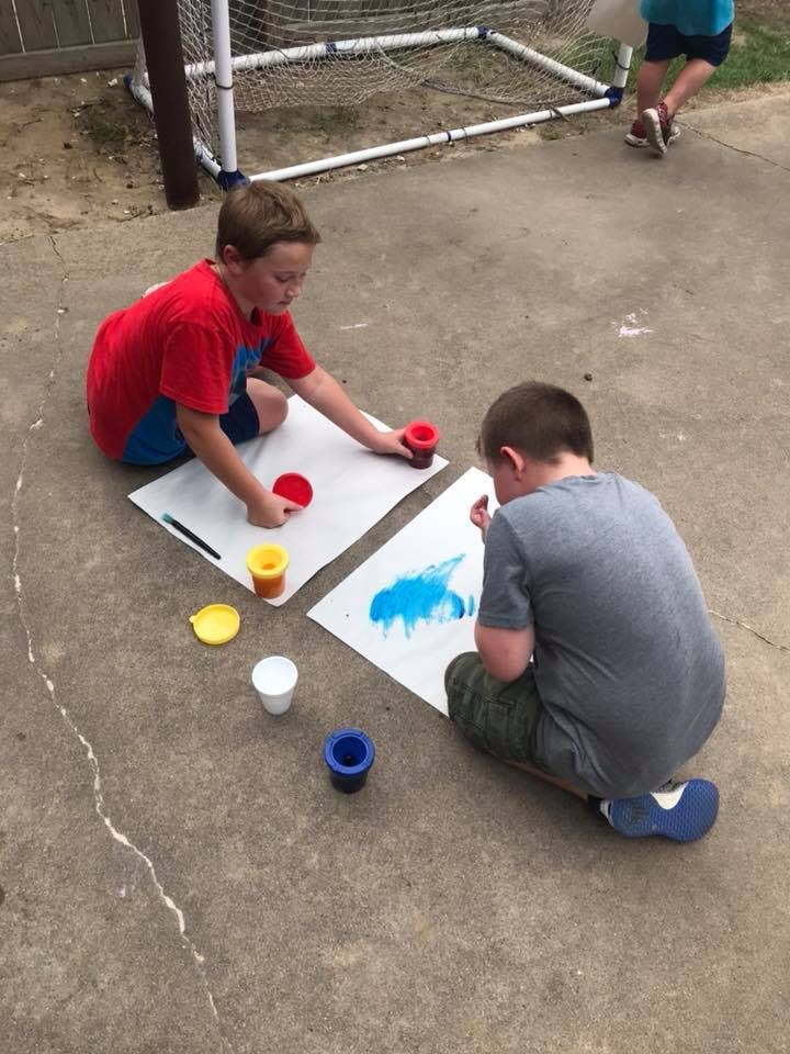 Two children painting on paper outdoors