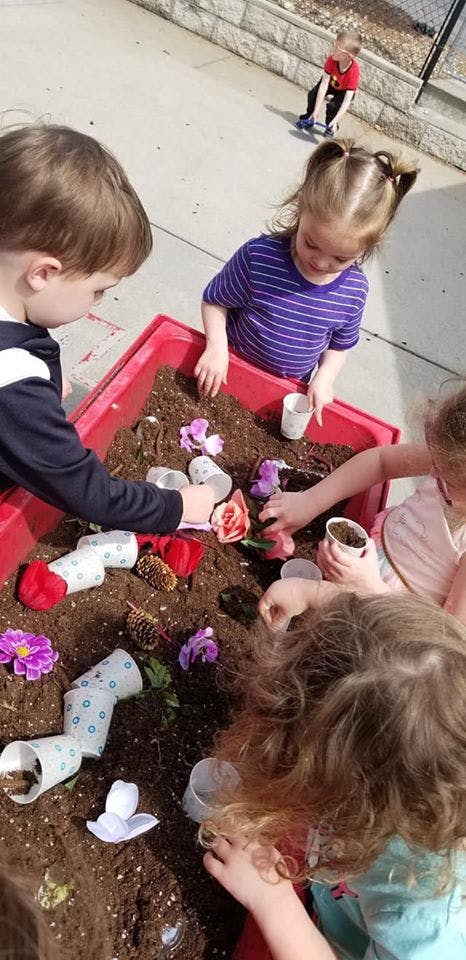 Children playing in a red bin filled with dirt and artificial flowers