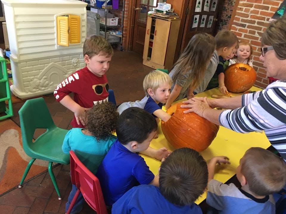 Adult and children gathered around a table with pumpkins