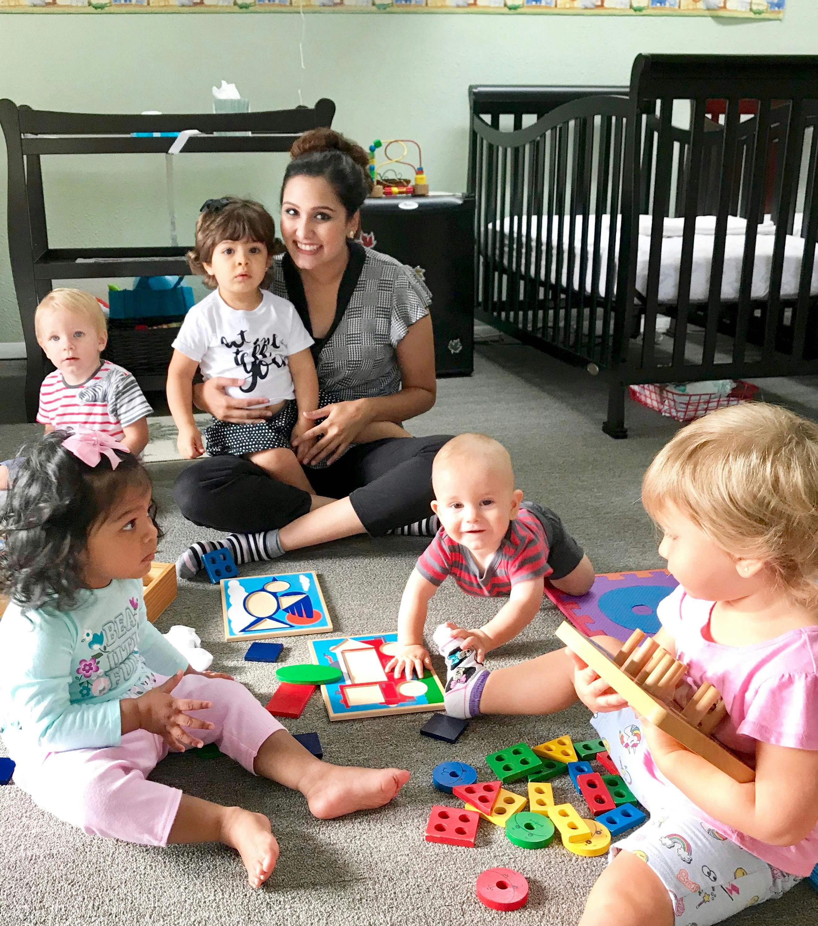 Adult and multiple children playing with toys on the floor in a room with cribs