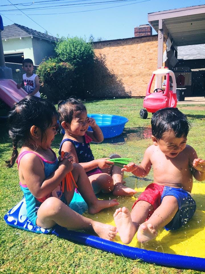 Three children playing on a yellow splash pad in a yard