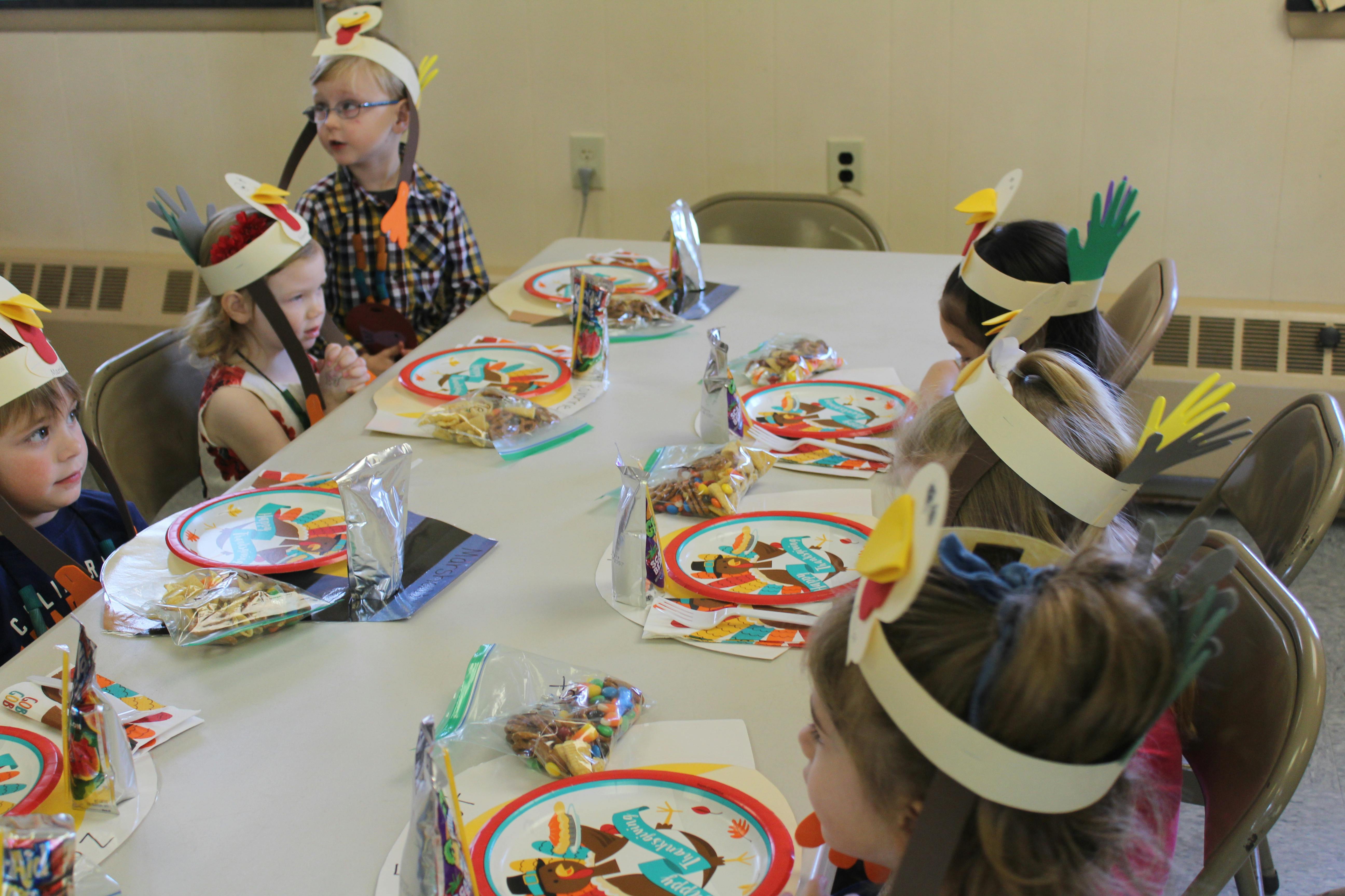 Children wearing paper turkey hats sitting at a table with plates