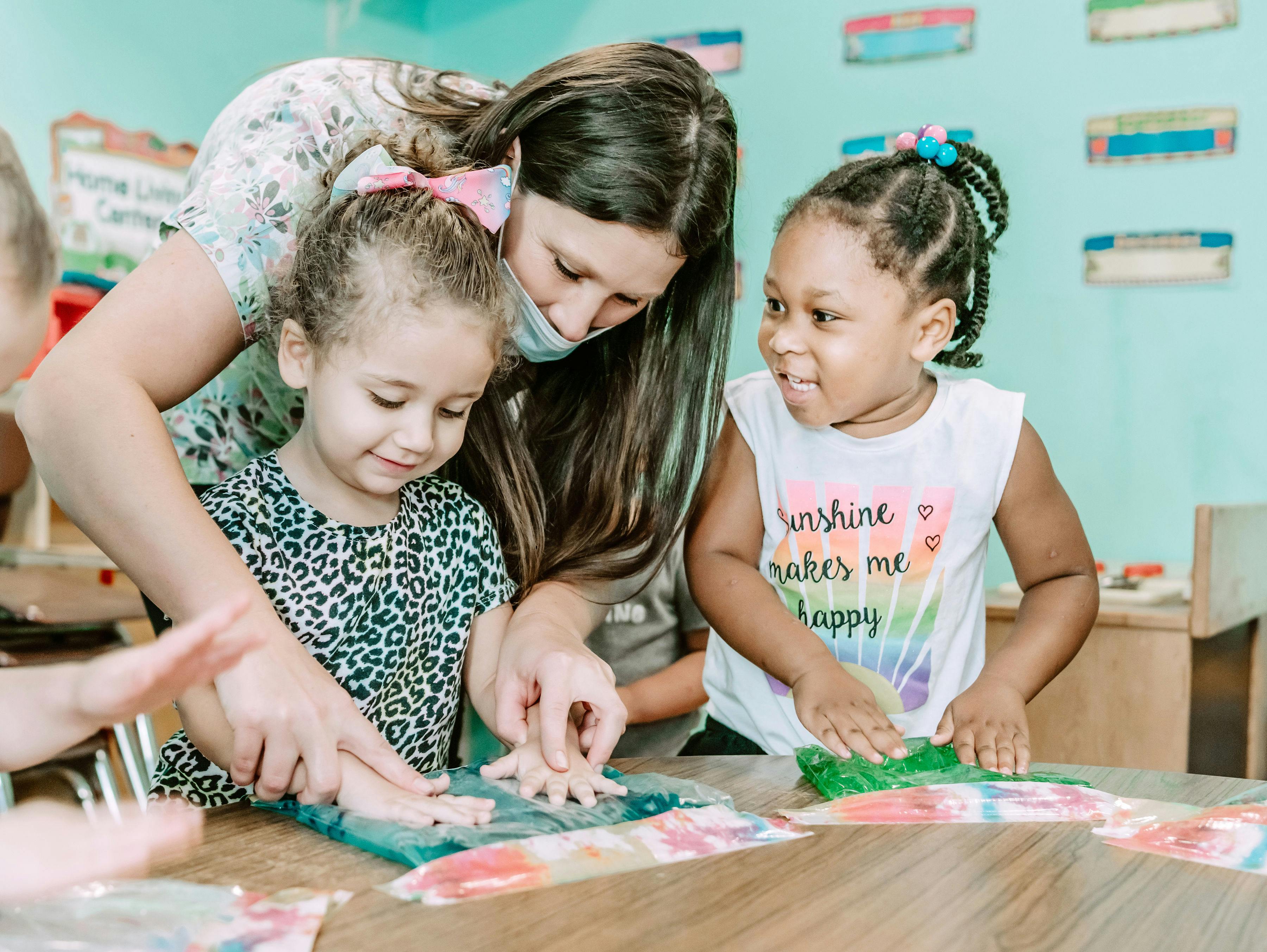 Adult and two children doing an art activity at a table in a classroom