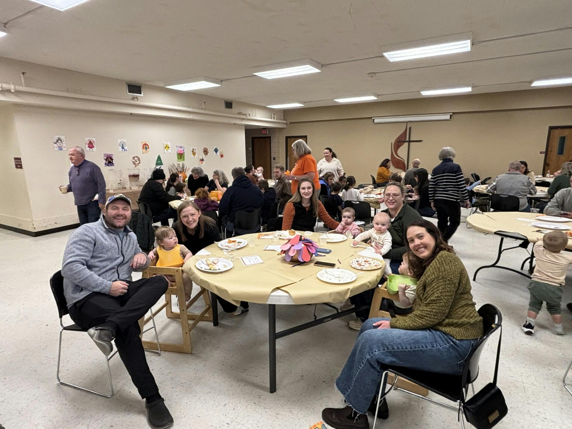 People gathered around tables, some with young children, in a large room