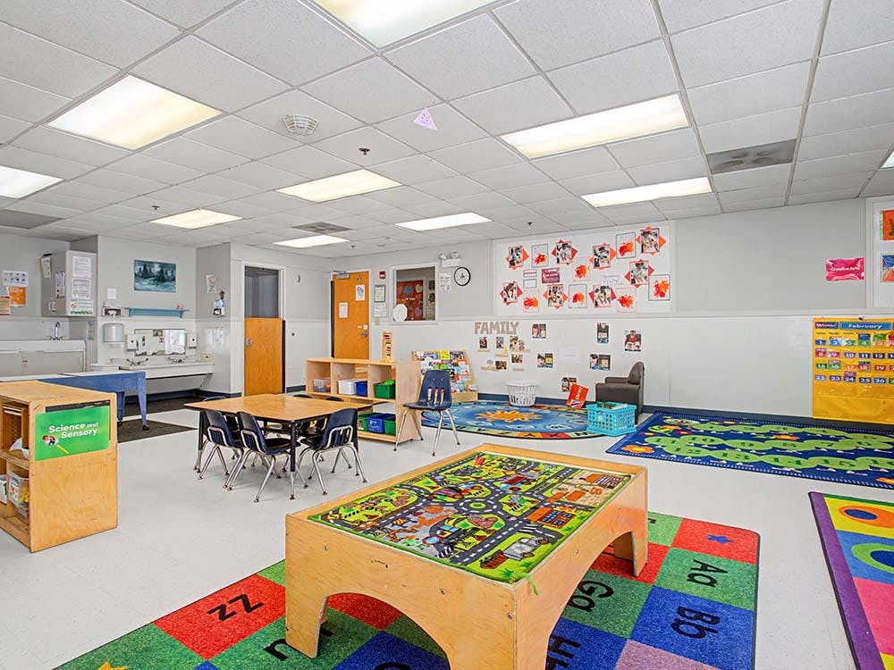 Classroom with small tables and chairs, play mats, and a play table